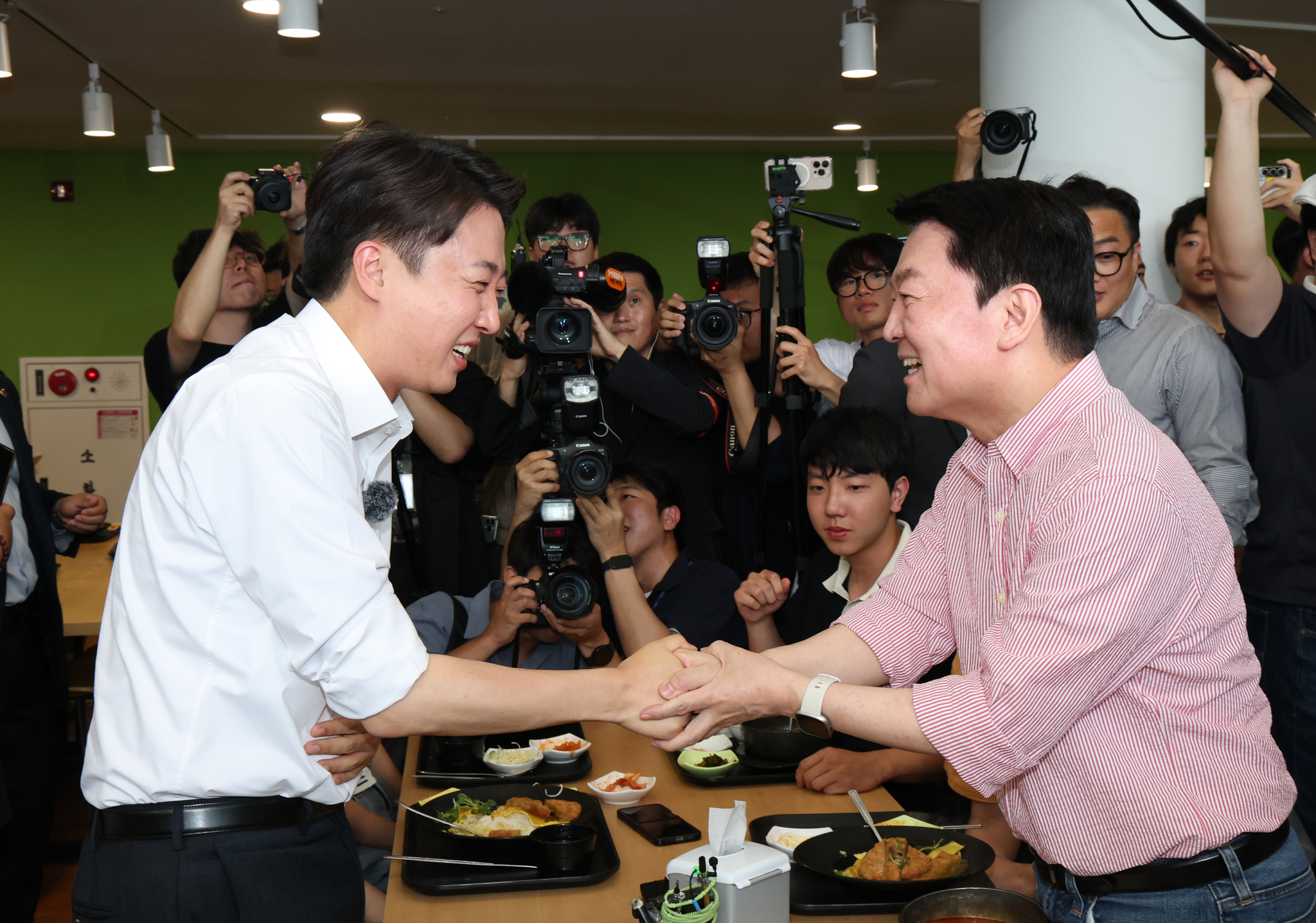 Reform Party candidate Lee Jun-seok, left, shakes hands with Rep. Ahn Cheol-soo, co-chair of the People Power Party's election committee, at a cafeteria inside the campus of Gachon University in Seongnam, Gyeonggi, on May 21. [NEWS1] 