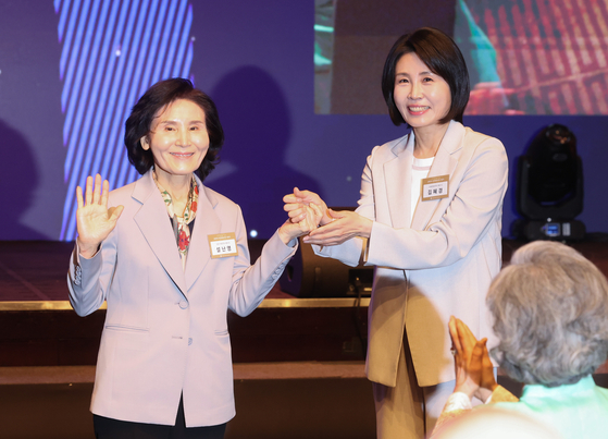 Kim Hye-kyung, the spouse of Democratic Party presidential candidate Lee Jae-myung, right, and Seol Nan-young, the spouse of People Power Party candidate Kim Moon-soo, hold hands during the 70th anniversary ceremony of the Jogye Order’s central laity association at the Shilla Hotel in Jung District, central Seoul, on May 12. [YONHAP]