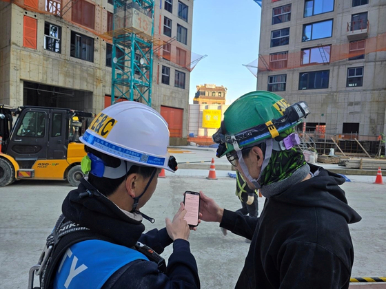 A DL E&C employee guides a foreign worker at an apartment construction site in the Seoul metropolitan area through an AI-based automatic translation system on Dec. 10, 2024. [YONHAP]