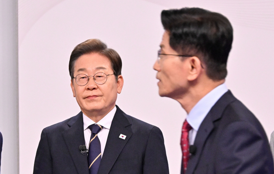 Democratic Party presidential candidate Lee Jae-myung, left, listens as People Power Party presidential candidate Kim Moon-soo speaks during the first presidential election debate at the SBS Sangam-dong studio in Mapo District, western Seoul on May 18. [JOINT PRESS CORPS] 