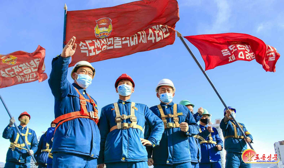 North Korean shock troops hold up flag while participating in the construction of 10,000 homes in the Hwasong area in Pyongyang. [RODONG SINMUN]    