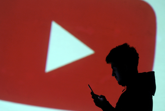A silhouette of a mobile user is seen next to a screen projection of Youtube logo in this picture illustration taken March 28, 2018. [REUTERS/YONHAP]