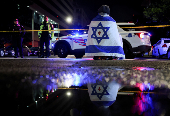 A man, with an Israeli flag with a cross in the center, looks on next to police officers working at the site where, according to the U.S. Homeland Security Secretary, two Israeli embassy staff were shot dead near the Capital Jewish Museum in Washington on May 21. [REUTERS/YONHAP]