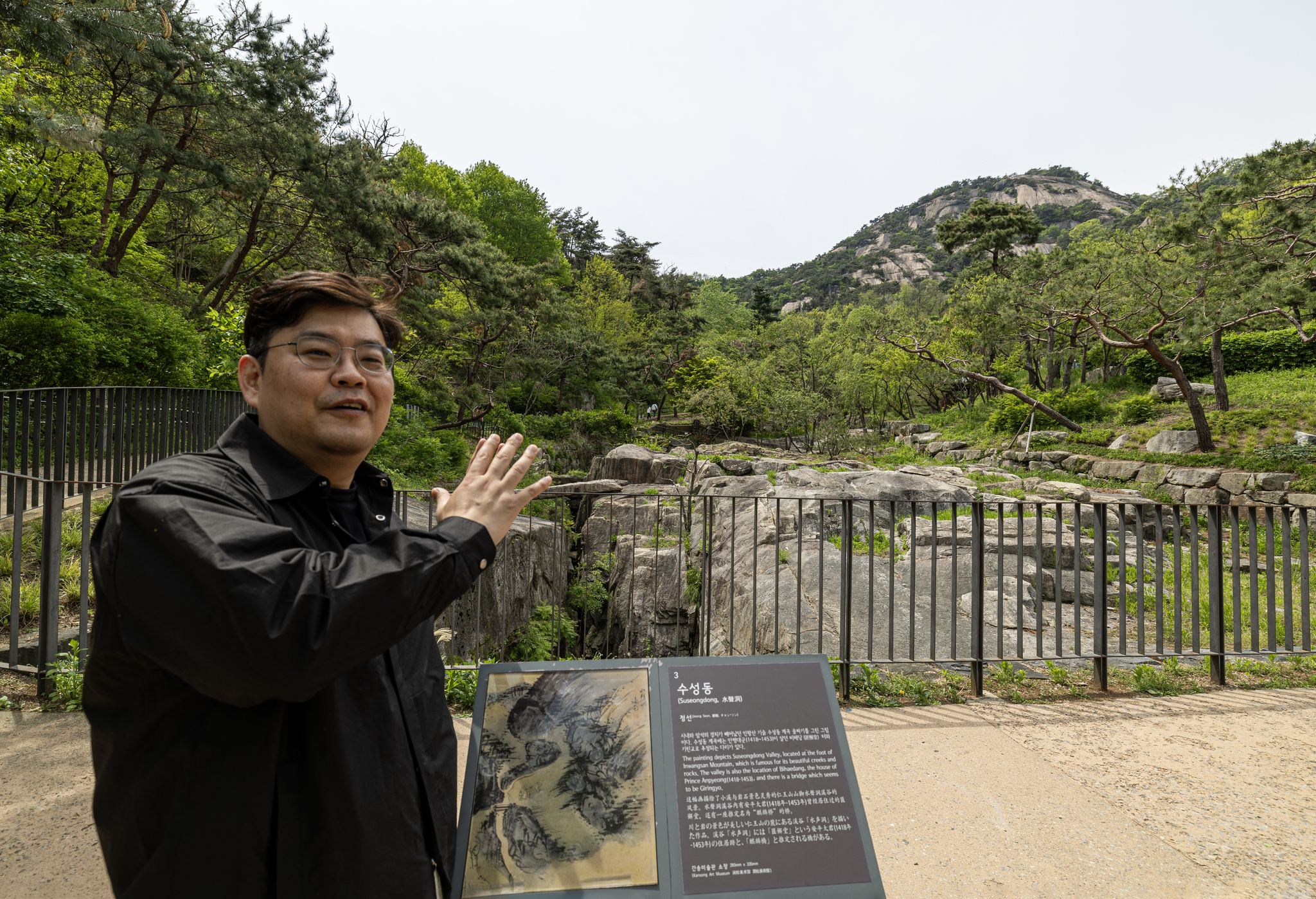 Jo Ji-yoon, curator at the Leeum Museum of Art, explains and compares Jeong Seon’s painting with the current landscape at Suseong-dong Valley on Mount Inwang in Jongno District, central Seoul, on May 2. [JOONGANG ILBO]