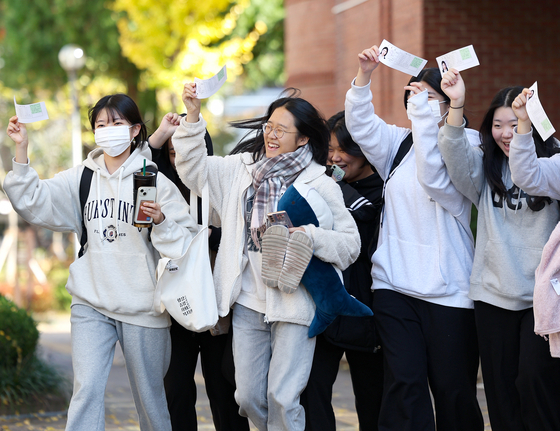 Students taking the College Scholastic Ability Test smile while holding their exam identification slips at a high school in Daegu on Wednesday, the day before the exam. [YONHAP]