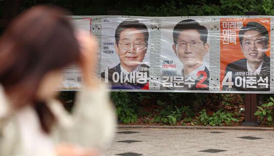 A pedestrian walks by presidential candidates' campaign posters attached to a wall in Mapo District, western Seoul, on May 23. [YONHAP]