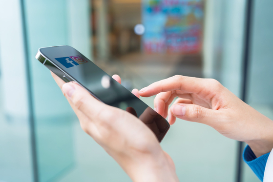 A person holds up a mobile phone in this stock image. [JOONGANG ILBO]
