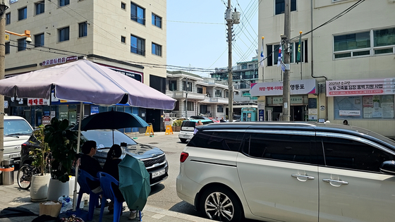 Two individuals claiming to monitor the election sit outside an early voting station in Yeongdeungpo District, western Seoul, filming voters, on May 30. They installed a shade tent near the site and alleged possible manipulation of the early voting process. [JOONGANG ILBO]