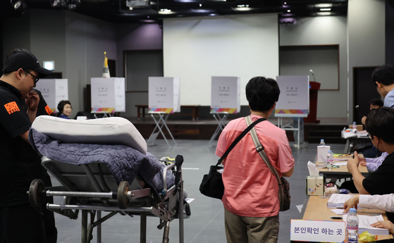 A patient casts a ballot with the help of a caregiver and paramedics at the Hannam No. 3 Polling Station, located at the Jungbu Technical Education Center in Yongsan District, central Seoul, on June 3, the day of the 21st presidential election. [YONHAP] 