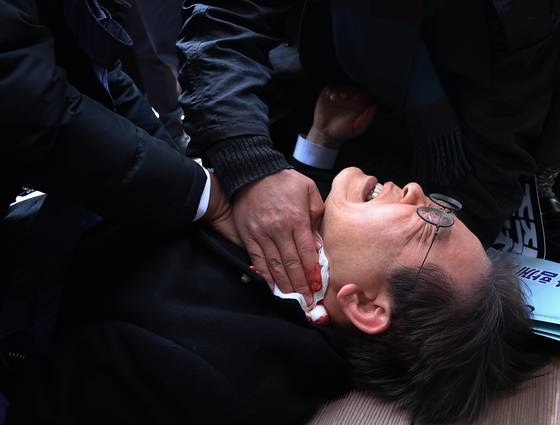 Lee Jae-myung is seen on the ground after being stabbed during his visit to the site of the new international airport on Gadeok Island, Busan, on Jan. 2 in last year. [YONHAP]