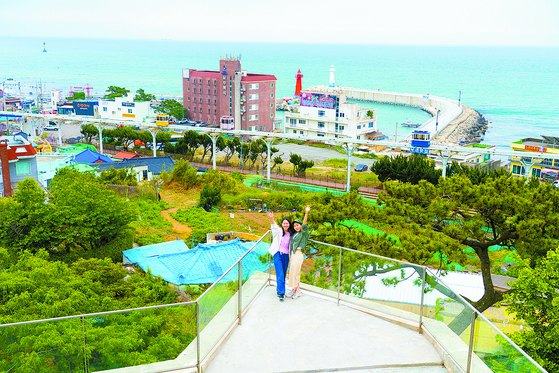 A Taiwanese mother and daughter pair take a photo with the Sky Capsule and Cheongsapo twin lighthouses in the background in Busan. [BAEK JONG-HYUN]