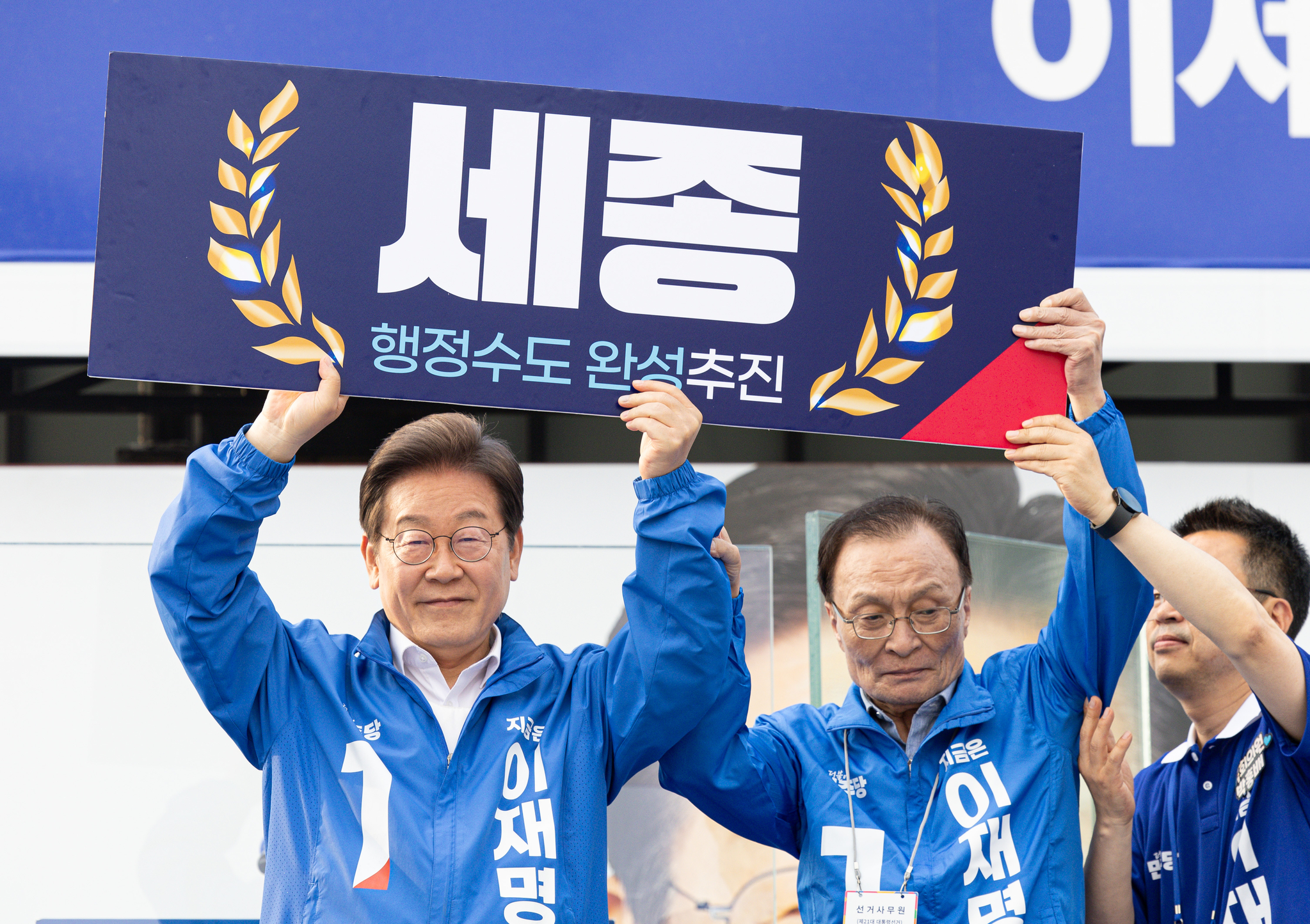 President Lee Jae-myung, left, then the Democratic Party presidential candidate, holds a placard calling to "complete" Sejong's creation as an administrative capital with former Rep. Lee Hae-chan during his campaign in the city last month. [NEWS1]
