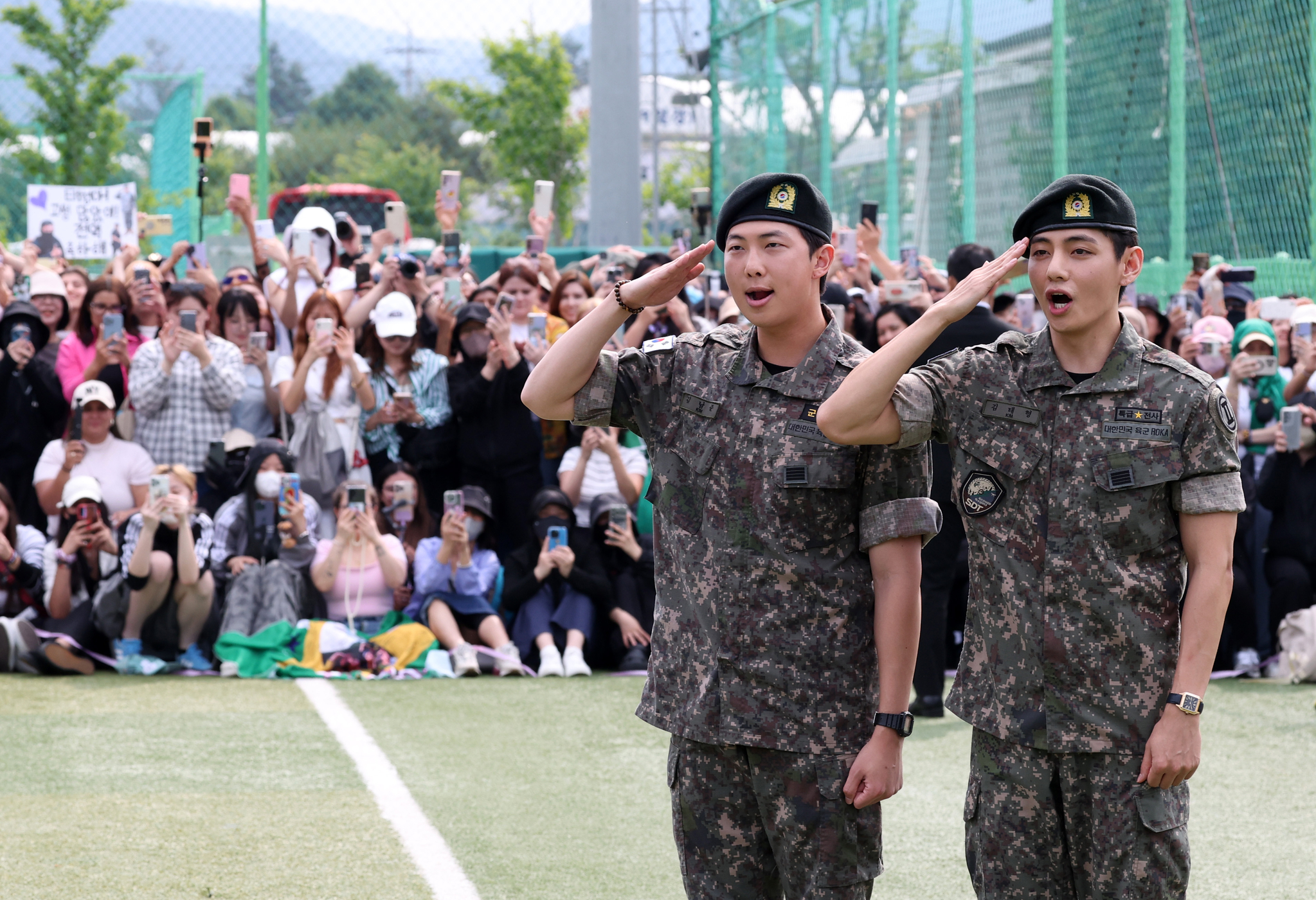 Members RM, left, and V of boy band BTS salute to fans after finishing their military duties on June 10 in Gangwon. In the back are fans who waited to congratulate the two singers on their big day. [YONHAP]