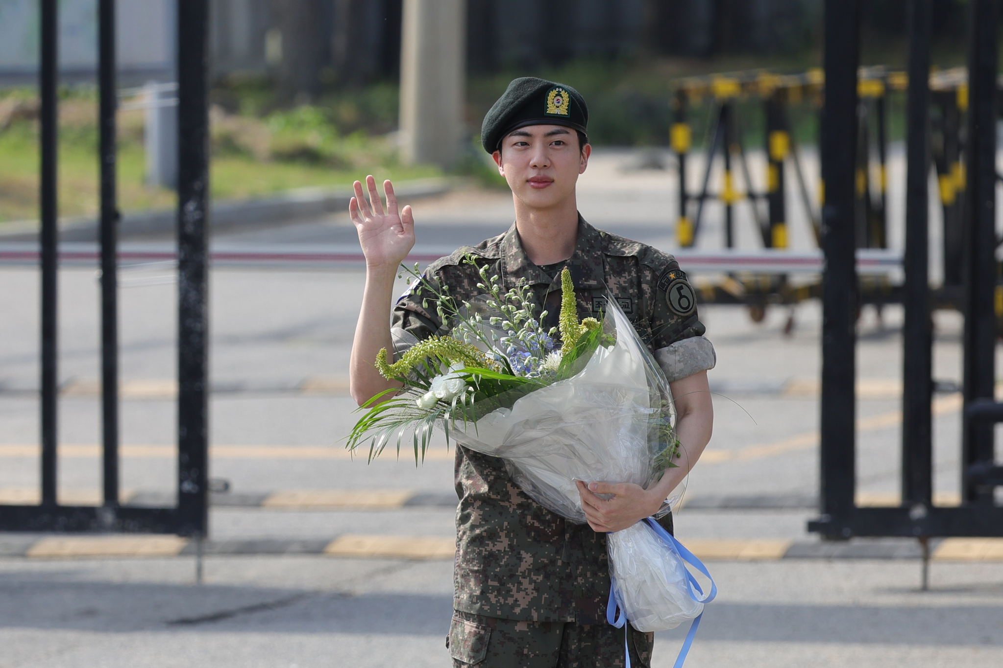 BTS's Jin, with a bouquet in his hand, waves at dozens of cameras as he gets discharged from the ROK Army 5th Infantry Division Recruit Training Center in Yeoncheon County, Gyeonggi, on June 12, 2024, after completing 18 months of mandatory military service. [YONHAP]