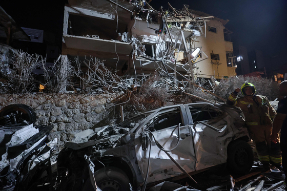 An Israeli firefighter stands next to a destoryed car at a site hit by a missile fired from Iran, in Ramat Gan on the outskirts of Tel Aviv on June 13. [AFP/YONHAP]