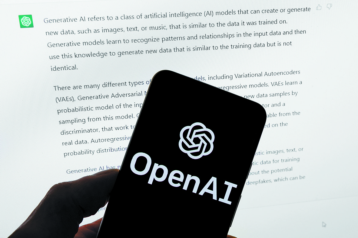The OpenAI logo is seen on a mobile phone in front of a computer screen displaying output from ChatGPT. [AP/YONHAP]