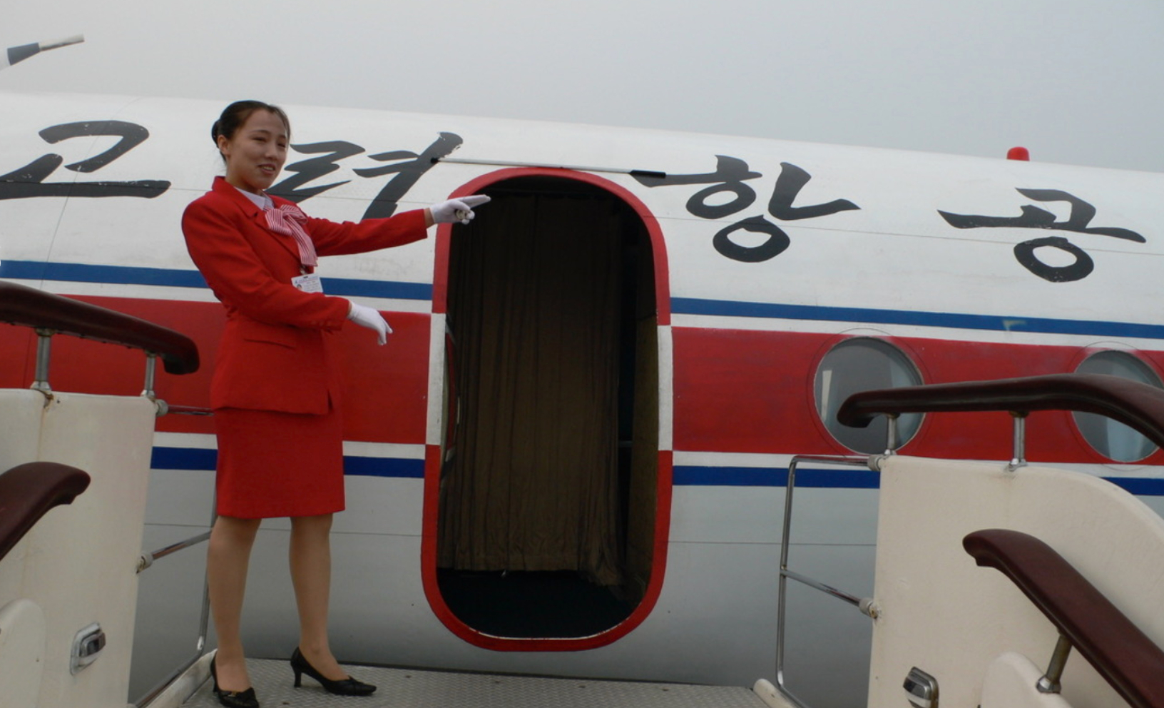 An undated image of a North Korean flight attendant pointing to a North Korean plane, posted on Koryo Tours' website [SCREEN CAPTURE]