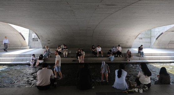 Citizens and tourists rest under the shade of a bridge on Cheonggye stream in Jongno District, central Seoul, on June 23. [YONHAP] 