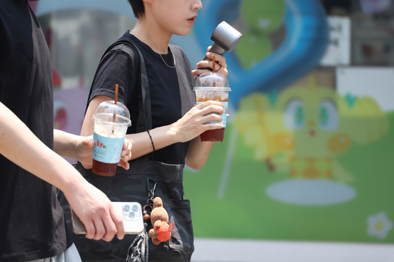 Citizens walk by a downtown area in Daegu with iced coffee and portable electric fans as heat advisories were issued in the region on June 28. [YONHAP] 