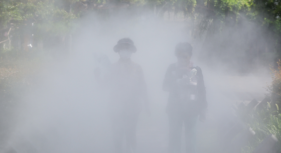 As cooling fog sprays from a mist system along a walking path in Jung District, Daegu, on June 30, people use handheld fans and personal fans to keep cool. [YONHAP] 