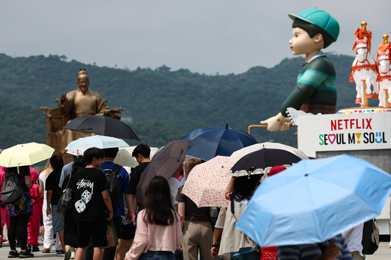 Tourists line up in front of a ″Squid Game″ experience zone under their parasols in Gwanghwamun, central Seoul, on July 4. [NEWS1]