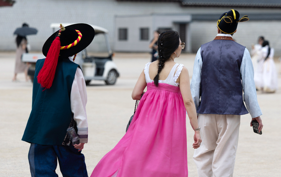 Tourists walk around the Gyeongbok Palace in central Seoul on July 2. One tourist, center, has taken off the long-sleeved jeogori top due to the heat. [NEWS1]