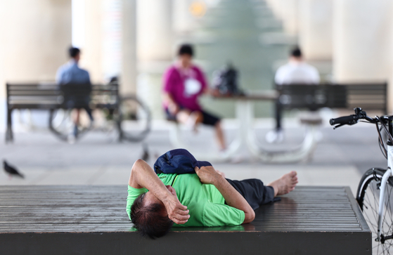 A citizen lies down at a bench at the Han River Park in Yeouido, western Seoul, on July 2. [NEWS1]