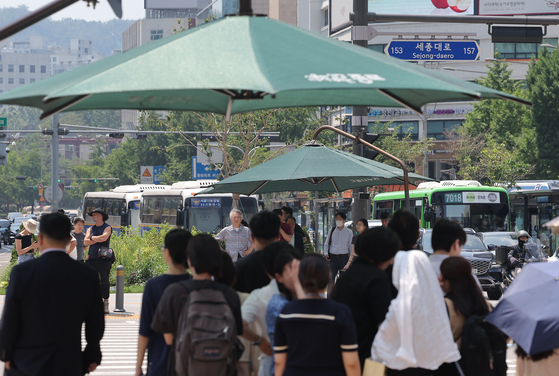 Citizens wait under the shade of a parasol on a street near Gwanghwamun Square in Jongno District, central Seoul on June 23. [YONHAP] 
