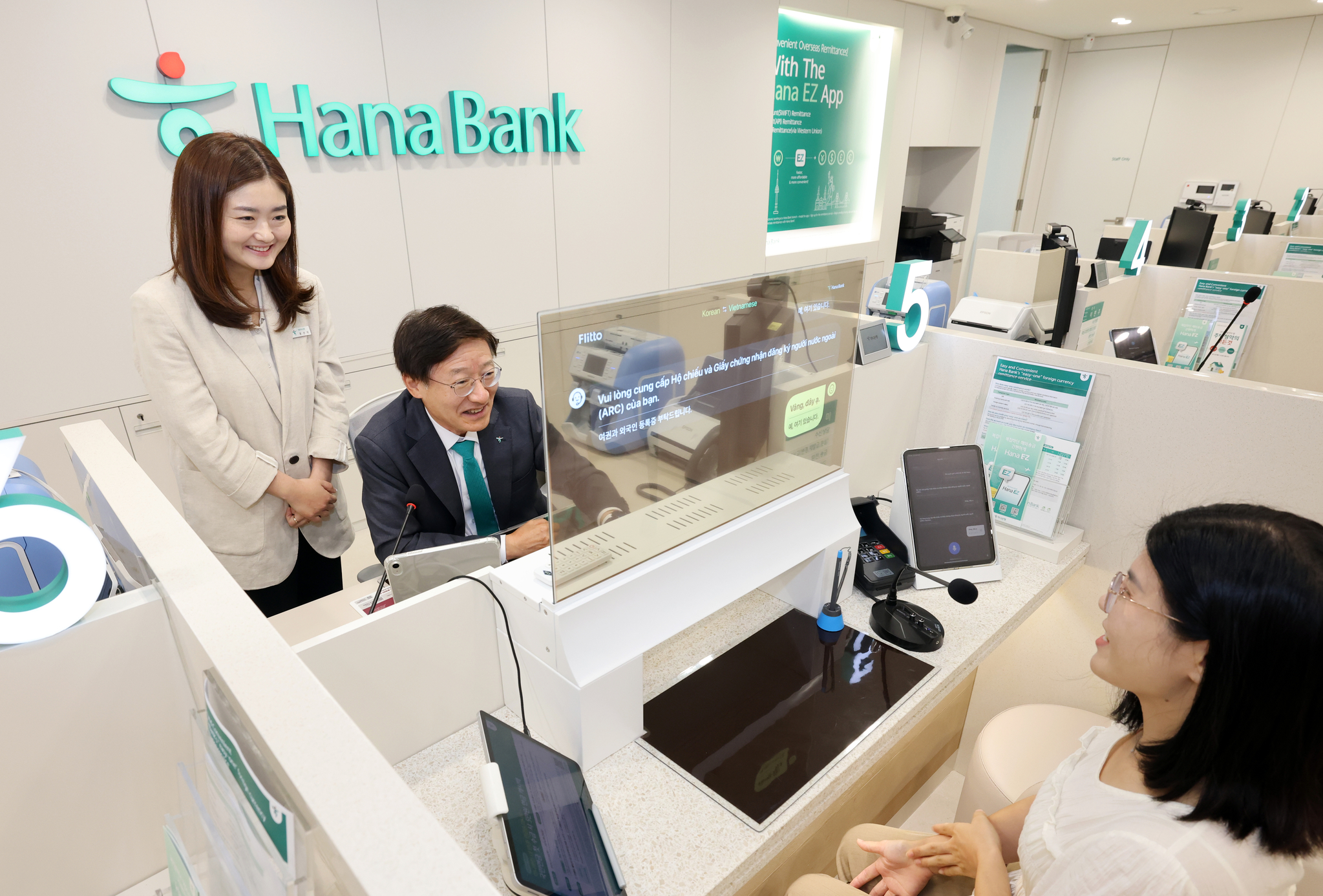 A foreign customer talks with bank tellers using a translation device. [HANA BANK]