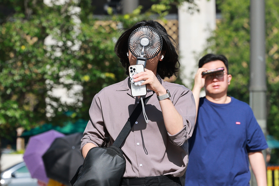 People walk in Jongno District, central Seoul, with portable electric fans amid heat advisories issued for most regions of Korea on July 10. [YONHAP] 
