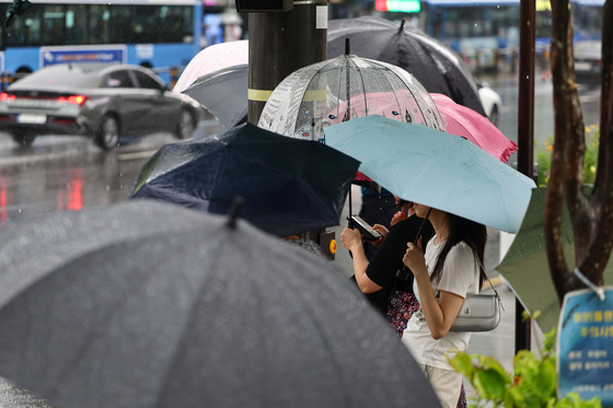 People wait at a crosswalk with umbrellas at Gwanghwamun Intersection in central Seoul on June 20, with a heavy rain advisory in effect across the city. [YONHAP]