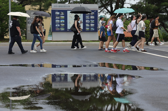 Tourists walk across rain-soaked ground with parasols at Imjingak in Paju, Gyeonggi on July 1. [YONHAP]