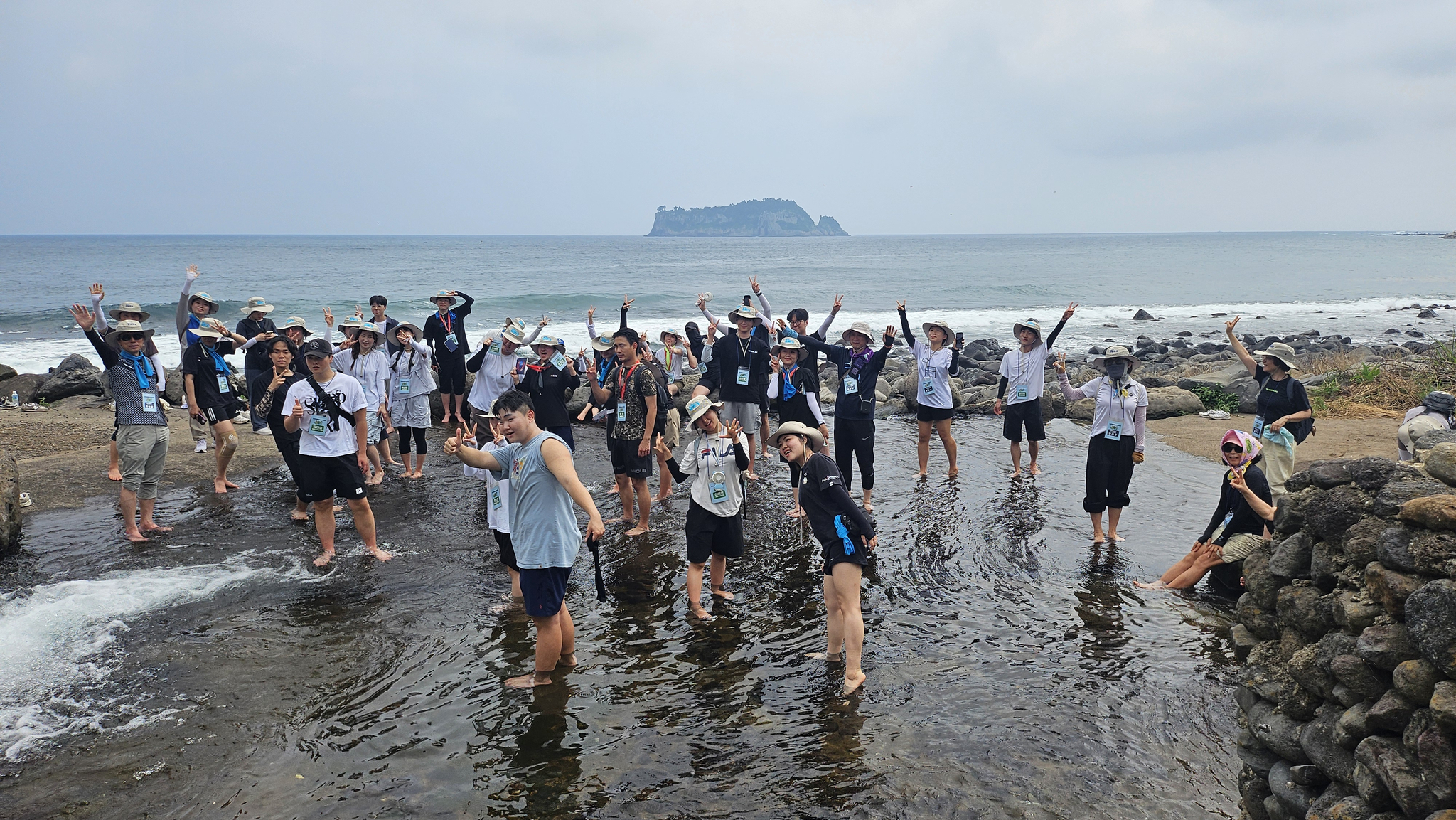 Participants of Jeju National University's 2025 learncation program pose for a photo at a beachside wading area. [JEJU NATIONAL UNIVERSITY]