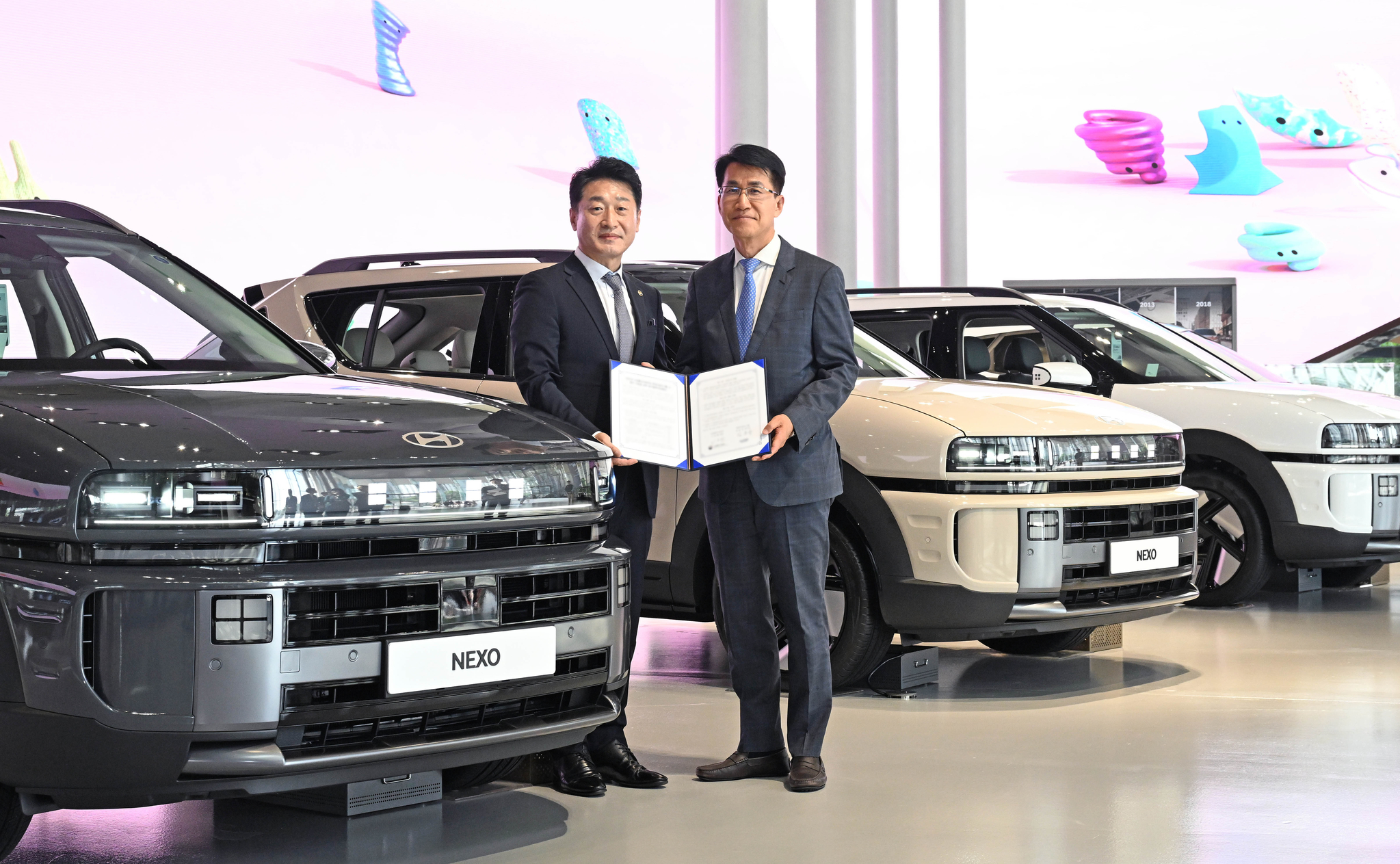 Kim Dong-wook, right, head of strategic policy division at Hyundai Motor Group, and Lee Ho-hyeon, second vice minister of trade, industry and energy, pose for a photo next to Nexo hydrogen cars after signing a fleet provision agreement in Goyang, Gyeonggi on July 22. [HYUNDAI MOTOR]