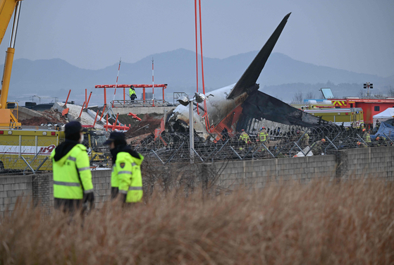Police officers stand guard as firefighters and recovery teams work at the scene where a Jeju Air Boeing 737-800 series aircraft crashed and burst into flames at Muan International Airport in Muan, South Jeolla on Dec. 30, 2024. [AFP/YONHAP] 