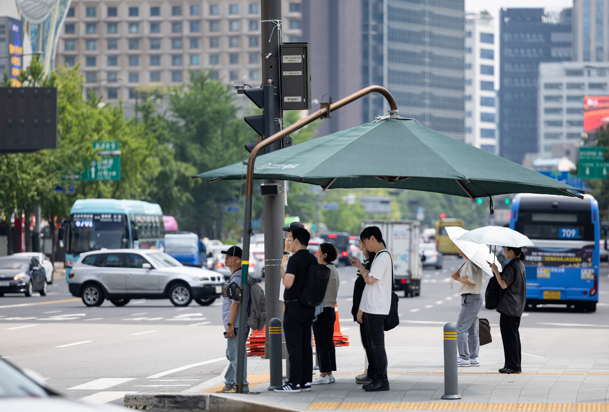 People take shelter from the heat under parasols at Gwanghwamun Square in central Seoul on July 25 as a heat wave warning remains in effect for most parts of Korea. [JOONGANG ILBO]