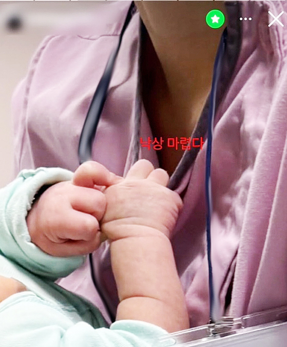 A nurse for the Daegu Catholic University Medical Center holds up a baby with the caption ″I’m itching to let one fall″ in a social media post that began circulating on Apr. 1. [SCREEN CAPTURE]