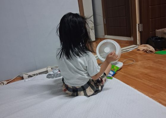A 6-year-old girl sits in front of a mini fan after playing with water to fall asleep on a sweltering night. Her mother says she still wakes up at night complaining about the heat. [JOONGANG ILBO]