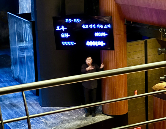 A sign language interpreter and an LED screen featuring the sounds of the noises being made on stage with diffferently stylized fonts are present during an accessible performance of the "Sammaekyung" at the Myeongdong Theater in Jung District, central Seoul, on Saturday. [LEE JIAN]
