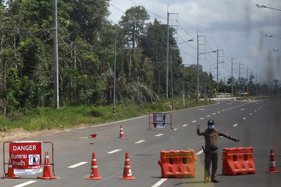 A picture taken through a window shows a Thai police officer standing guard next to an explosive danger sign on a main road in the Kantharalak District of Sisaket Province on Aug. 1.  [EPA/YONHAP]