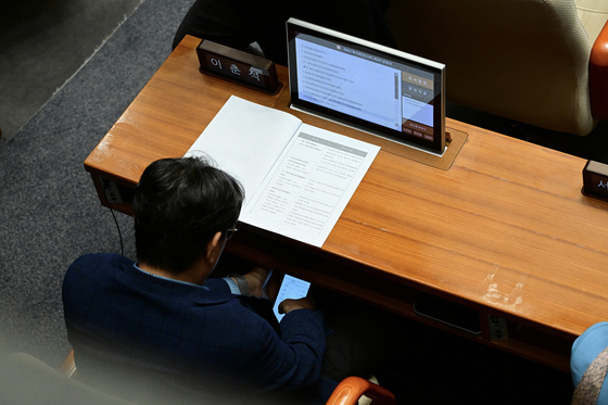Rep. Lee Choon-suak of the Democratic Party, who chairs the National Assembly’s Legislation and Judiciary Committee, appears to check a trading account registered to another person’s name during a plenary session at the National Assembly in Yeouido, western Seoul, on Aug. 4. [THE FACT]