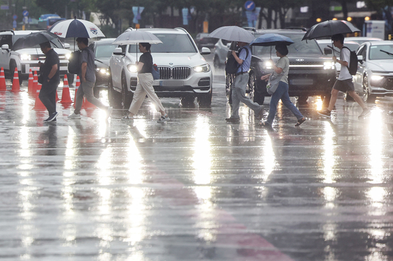 Commuters hurry across Gwanghwamun Intersection in Jongno District, central Seoul, on Aug. 13 as a heavy rain advisory is in effect for the capital. [NEWS1] 