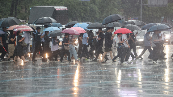 People cross a street in Jongno District, central Seoul, on Aug. 13 as heavy rainfall sweeps through central regions of the country. [YONHAP]