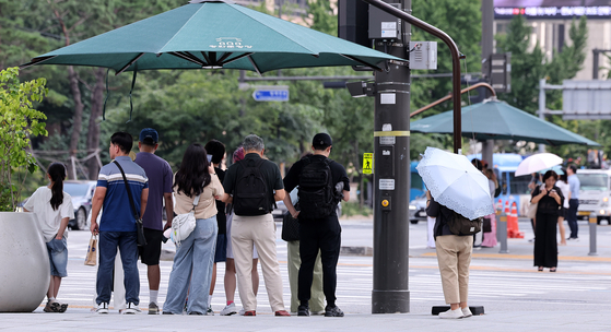 Pedestrians wait under the shade at a crossroad near Gwanghwamun in Jongno District, central Seoul, on Aug. 21. [NEWS1]