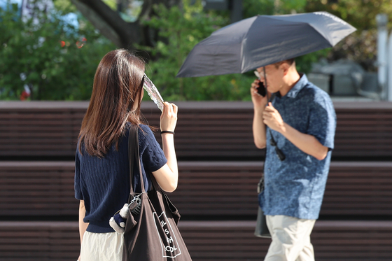 Pedestrians use parasols or fans to shade themselves as they walk on Gwanghwamun Square in Jongno District, central Seoul, on Aug. 21. [YONHAP] 