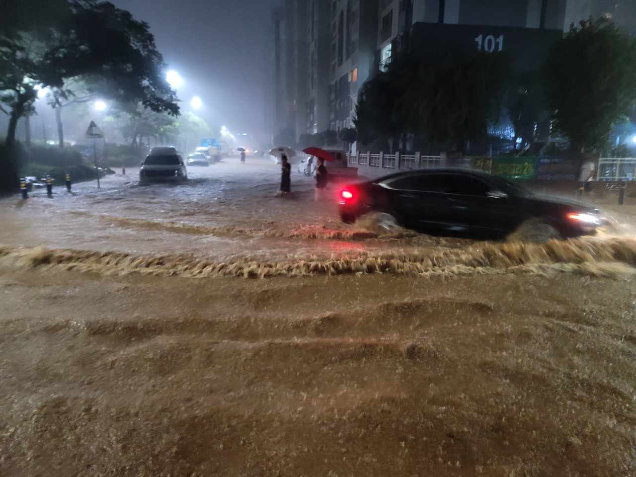 Passersby and vehicles navigate a road submerged by heavy rain in Muan, South Jeolla, on Aug. 3. [NEWS1] 