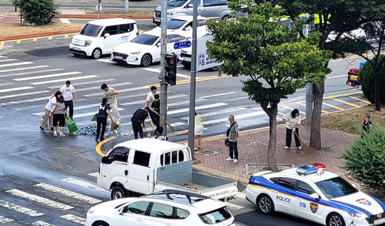 Daejeon Sports Council employees clean up beer bottles spilled from a delivery truck at the Chungmu-ro intersection in Daeheung-dong, Jung District, Daejeon, at around 10:20 a.m. on Aug. 29. [NEWS1]