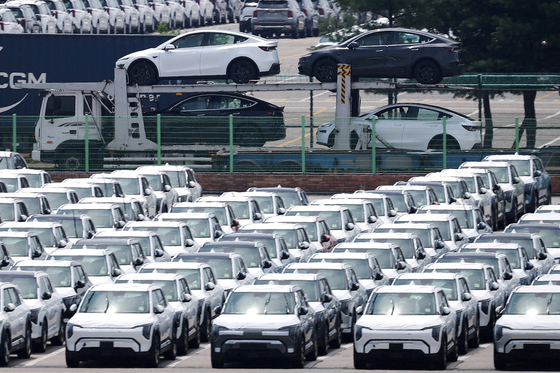 A car carrier transporting Tesla vehicles travels past Kia Motors' vehicles parked at a port in Pyeongtaek, Gyeonggi, on July 31. [REUTERS/YONHAP] 