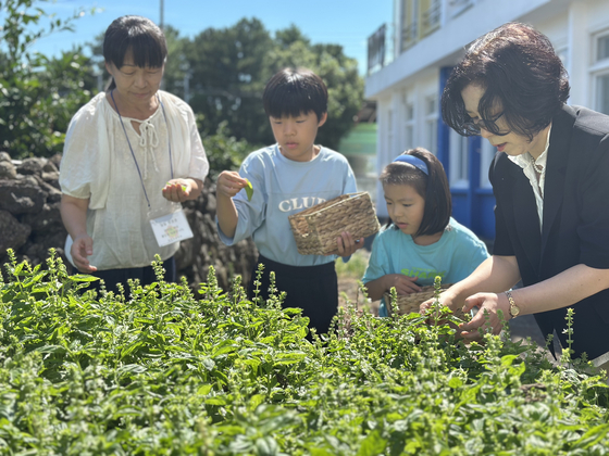 Siblings Kim Geon-hu, center left, and Kim A-rang, center right, who came to Changcheon Elementary School in Jeju through the rural school exchange program, pick basil grown by students in the school garden with their mother, left, and the principal on Aug. 28. [CHOI CHOONG-IL]