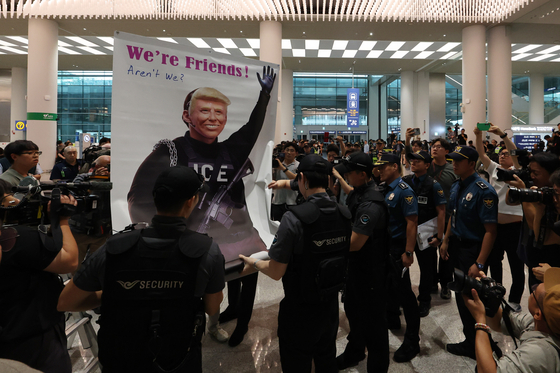 On Sept. 12, as Korean workers detained by U.S. Immigration and Customs Enforcement authorities in Georgia returned home, airport police block a protest by a civic group holding a banner with the face of U.S. President Donald Trump with the caption, ″We're friends! Aren't we?″ at the arrivals hall of Terminal 2 at Incheon International Airport. [YONHAP]